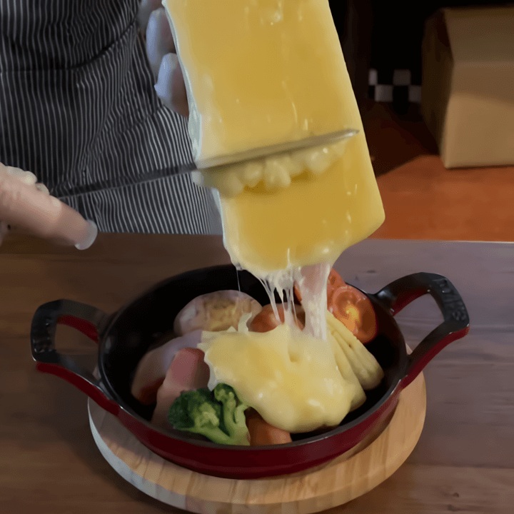 熱々の鉄板料理にたっぷりと削り落とされる濃厚なラクレットチーズ